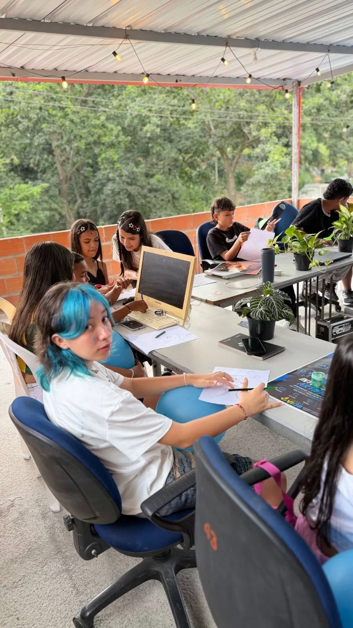 Estudiantes trabajando en la mesa larga de la terraza, junto al afiche del curso de inteligencia artificial